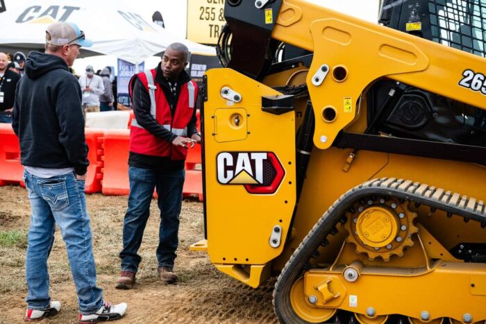 Equip Exposition attendee talking to Dante in the Caterpillar booth next to a compact track loader