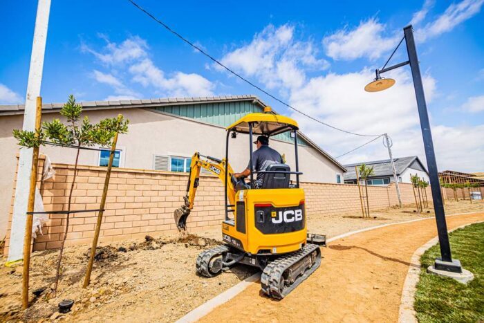 JCB mini excavator digging dirt nearish a building 