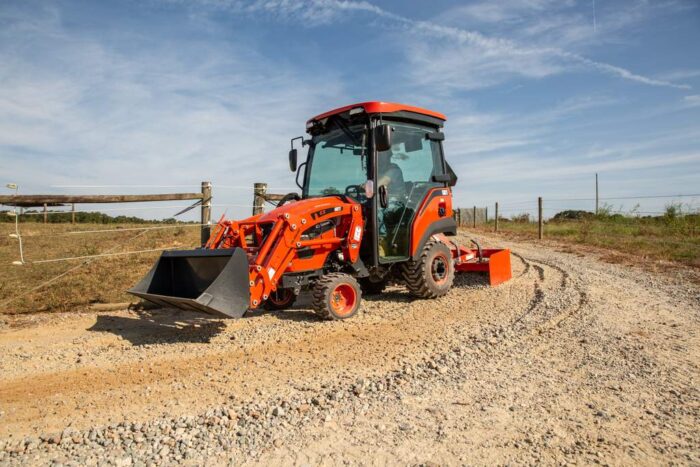 Kioti tractor with a cab and a landscape rake off the back on a dirt road