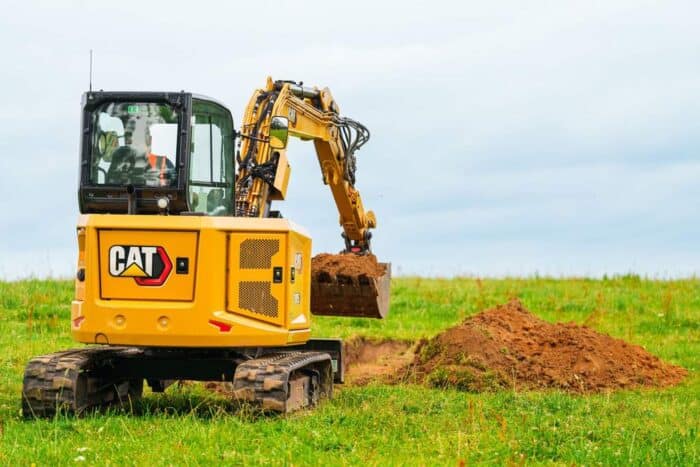 Caterpillar mini excavator digging in grass back shot